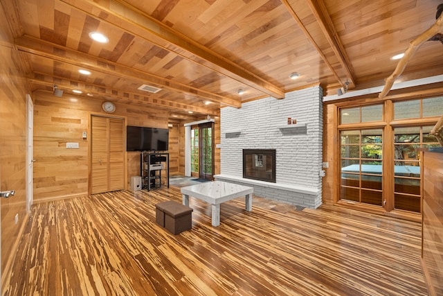 unfurnished living room featuring wood ceiling, wooden walls, wood-type flooring, beam ceiling, and a fireplace