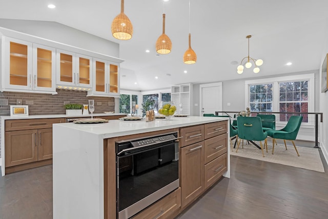 kitchen with an inviting chandelier, a center island with sink, wall oven, tasteful backsplash, and decorative light fixtures