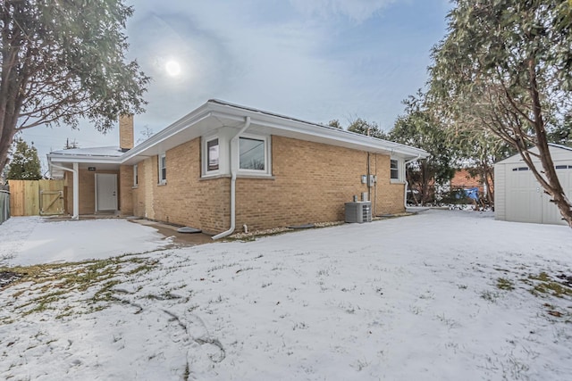 snow covered property featuring central AC unit and a storage shed