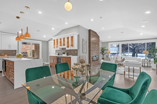 dining space featuring a large fireplace, beverage cooler, light hardwood / wood-style flooring, and lofted ceiling