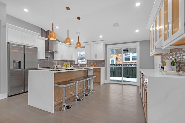 kitchen with decorative light fixtures, white cabinets, an island with sink, and stainless steel fridge with ice dispenser