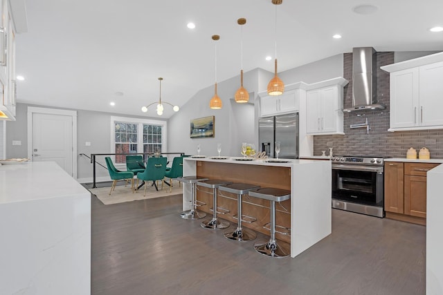 kitchen featuring white cabinetry, hanging light fixtures, a kitchen island with sink, appliances with stainless steel finishes, and wall chimney exhaust hood