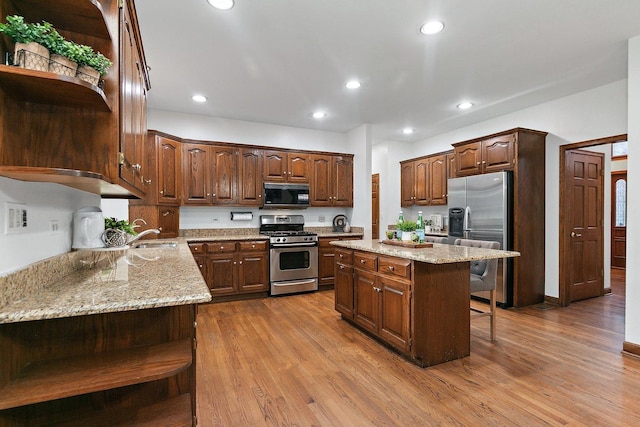 kitchen with light stone countertops, stainless steel appliances, a kitchen breakfast bar, wood-type flooring, and a kitchen island