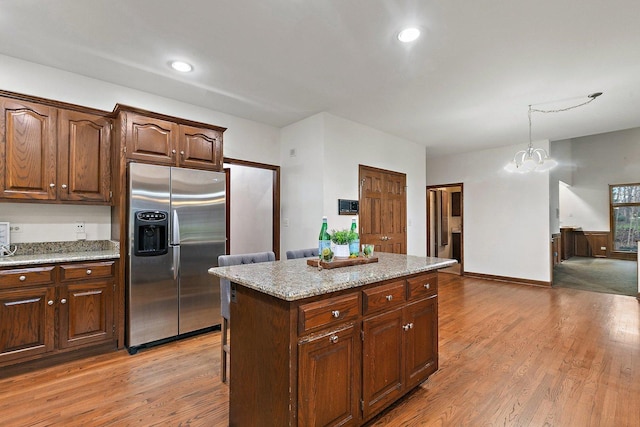 kitchen with a center island, stainless steel refrigerator with ice dispenser, a chandelier, decorative light fixtures, and light hardwood / wood-style floors