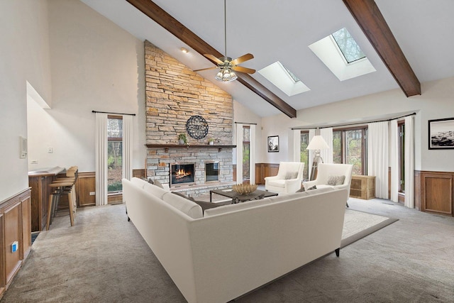 living room featuring high vaulted ceiling, a stone fireplace, ceiling fan, beam ceiling, and light colored carpet