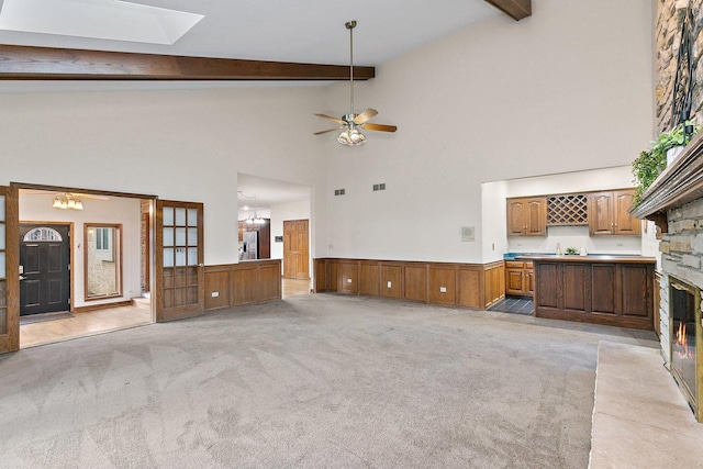 unfurnished living room with a skylight, beamed ceiling, high vaulted ceiling, light carpet, and ceiling fan with notable chandelier