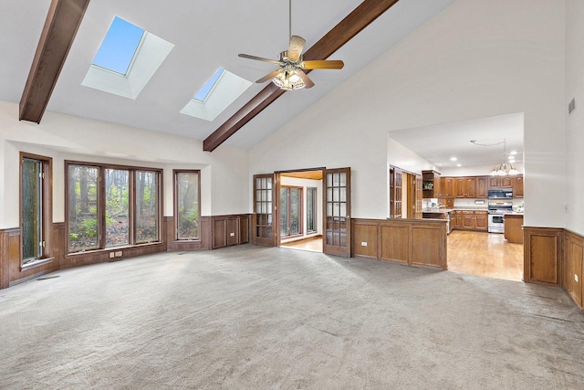 living room with light carpet, french doors, a skylight, ceiling fan with notable chandelier, and high vaulted ceiling