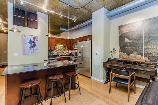 kitchen featuring stainless steel fridge, dark stone countertops, light wood-type flooring, and sink