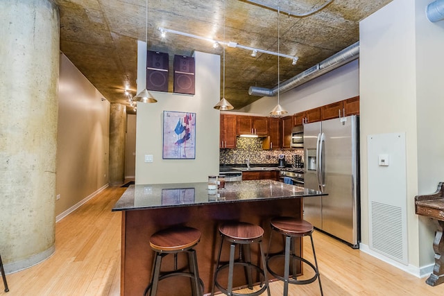 kitchen featuring stainless steel appliances, light hardwood / wood-style flooring, a breakfast bar area, and dark stone countertops