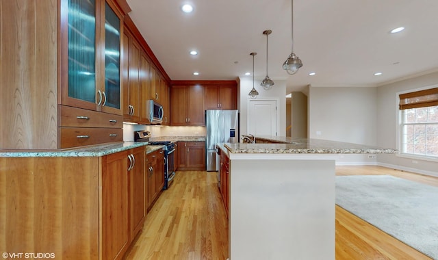 kitchen featuring decorative light fixtures, light wood-type flooring, stainless steel appliances, and an island with sink