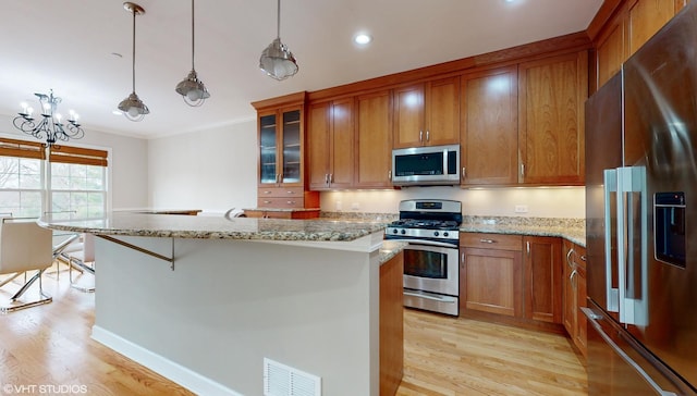 kitchen with light stone counters, light hardwood / wood-style flooring, decorative light fixtures, a kitchen bar, and appliances with stainless steel finishes