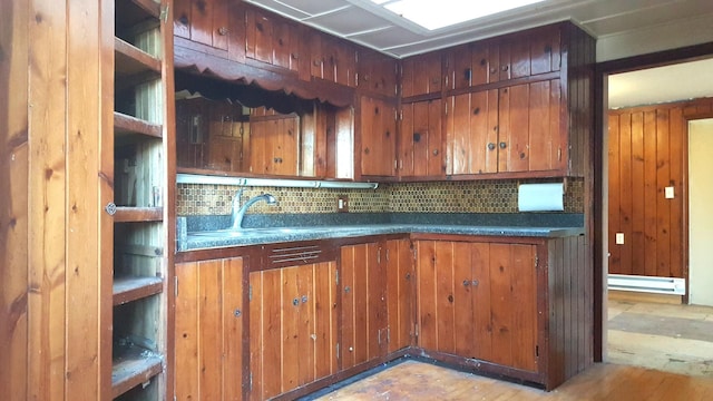 kitchen with brown cabinets, tasteful backsplash, baseboard heating, a sink, and wooden walls