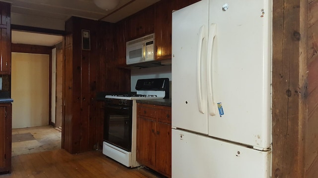 kitchen with white appliances, wood walls, dark countertops, and light wood-style floors