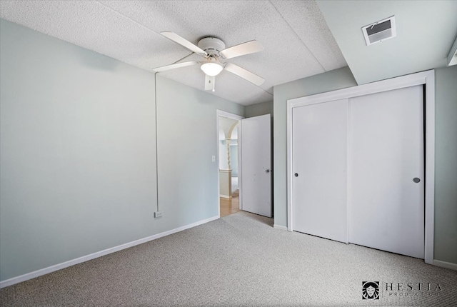 unfurnished bedroom featuring ceiling fan, a closet, light carpet, and a textured ceiling