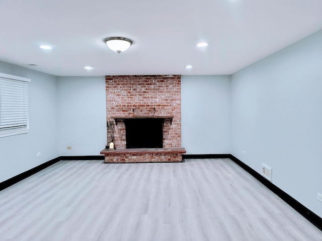 unfurnished living room featuring light hardwood / wood-style flooring and a brick fireplace