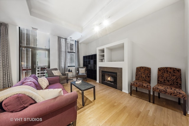 living room featuring built in shelves, light hardwood / wood-style floors, crown molding, and a tray ceiling