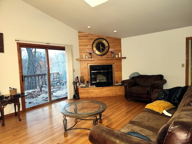 living room with a large fireplace, light hardwood / wood-style flooring, wooden walls, and vaulted ceiling