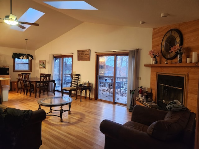 living room featuring wood walls, high vaulted ceiling, a skylight, light hardwood / wood-style flooring, and ceiling fan