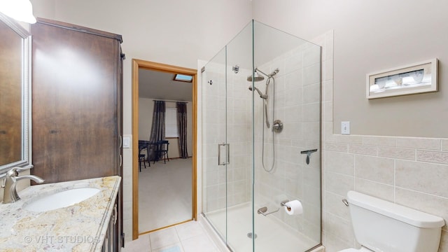 bathroom featuring vanity, tile patterned floors, toilet, tile walls, and a shower with shower door