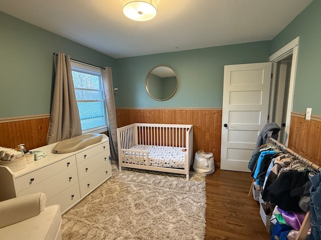 bedroom featuring a crib, hardwood / wood-style floors, and wooden walls