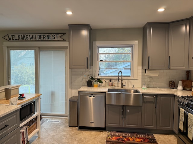 kitchen with gray cabinetry, light stone countertops, sink, backsplash, and appliances with stainless steel finishes