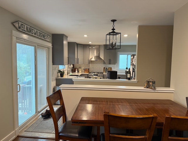 kitchen with hardwood / wood-style floors, wall chimney range hood, hanging light fixtures, decorative backsplash, and gray cabinets