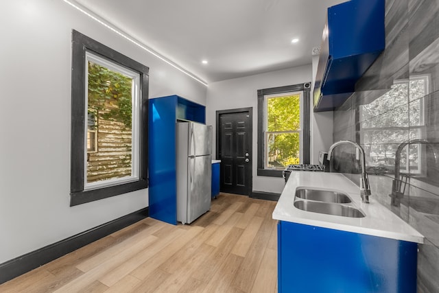 kitchen featuring light hardwood / wood-style floors, stainless steel refrigerator, blue cabinets, and sink