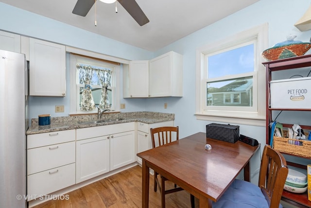 kitchen featuring sink, light hardwood / wood-style flooring, stainless steel fridge, light stone countertops, and white cabinets