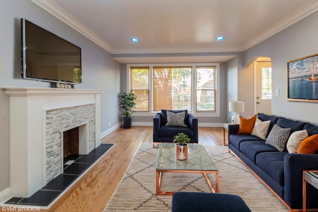 living room featuring a stone fireplace, crown molding, and wood-type flooring