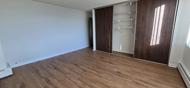 unfurnished bedroom featuring a textured ceiling, a baseboard heating unit, a closet, and dark hardwood / wood-style flooring