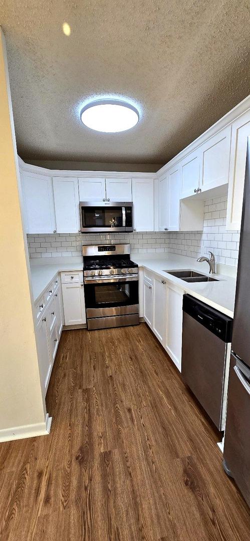 kitchen with dark wood-style floors, light countertops, appliances with stainless steel finishes, white cabinets, and a sink