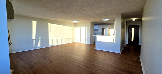 empty room with a textured ceiling, dark wood finished floors, and baseboards