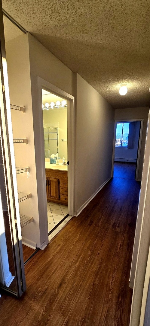 hallway with a textured ceiling, wood finished floors, and baseboards