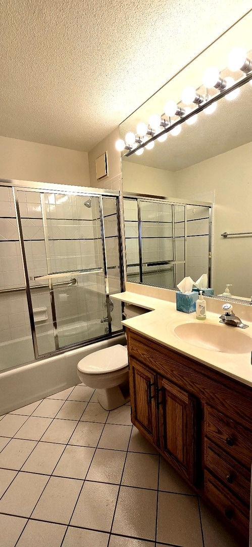 full bath featuring enclosed tub / shower combo, a textured ceiling, toilet, vanity, and tile patterned floors