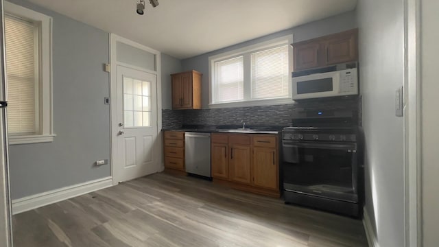 kitchen featuring sink, black gas range, backsplash, stainless steel dishwasher, and light wood-type flooring