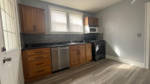 kitchen with sink, stainless steel dishwasher, black range with gas stovetop, hardwood / wood-style floors, and decorative backsplash