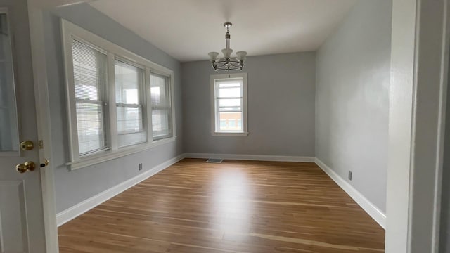 empty room with wood-type flooring and a chandelier