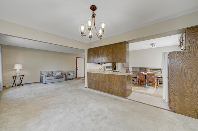 kitchen featuring white refrigerator, hanging light fixtures, a notable chandelier, light colored carpet, and kitchen peninsula