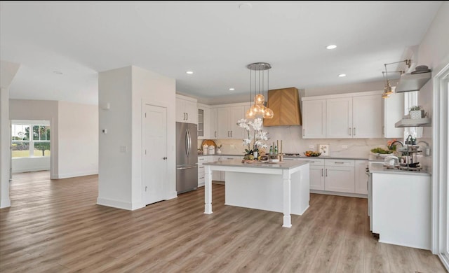 kitchen with white cabinets, a center island, light hardwood / wood-style floors, stainless steel refrigerator, and hanging light fixtures