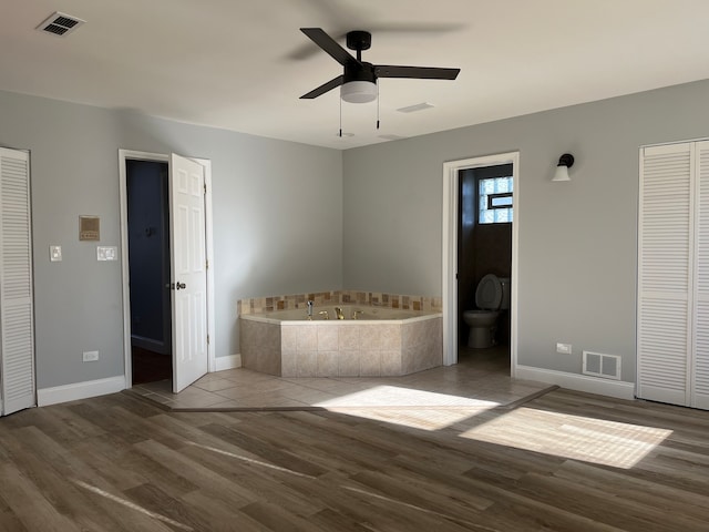 bathroom with tiled tub, ceiling fan, wood-type flooring, and toilet