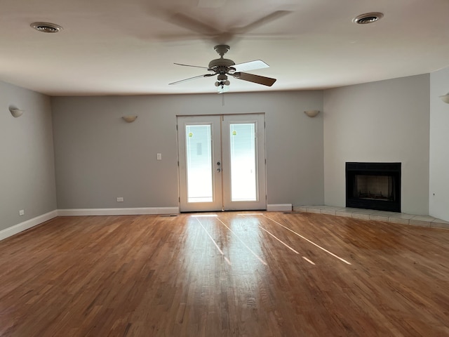 unfurnished living room with a tile fireplace, french doors, light hardwood / wood-style floors, and ceiling fan