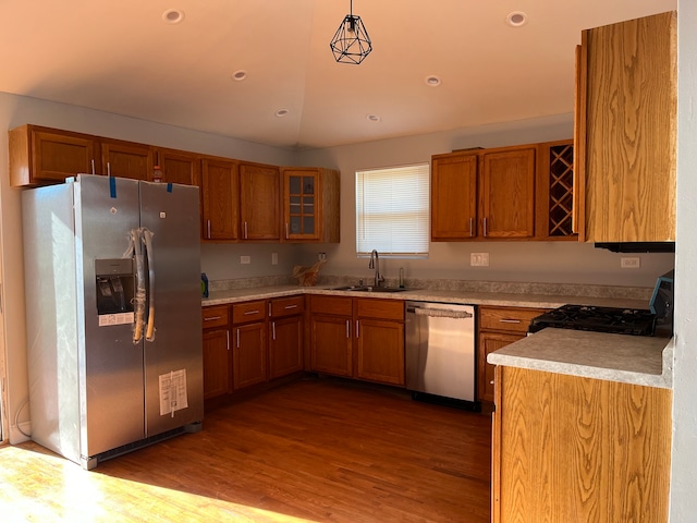 kitchen with stainless steel appliances, vaulted ceiling, sink, decorative light fixtures, and light hardwood / wood-style flooring