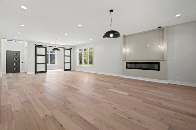 unfurnished living room with a barn door and light hardwood / wood-style flooring