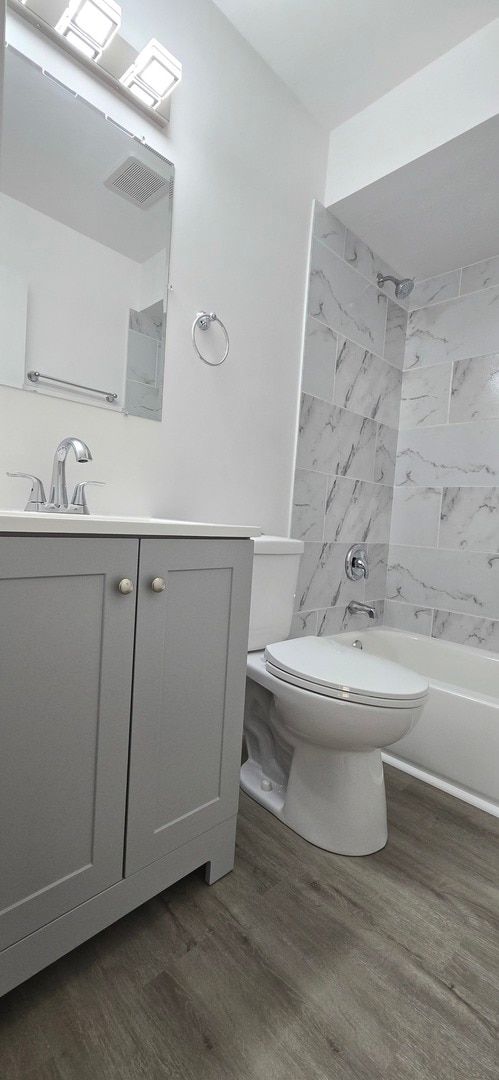 full bathroom with hardwood / wood-style floors, tiled shower / bath combo, toilet, and vanity