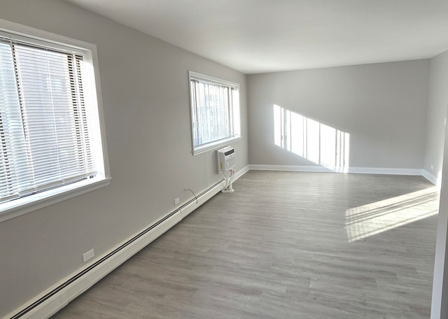 empty room featuring light wood-type flooring, a wall unit AC, and baseboard heating