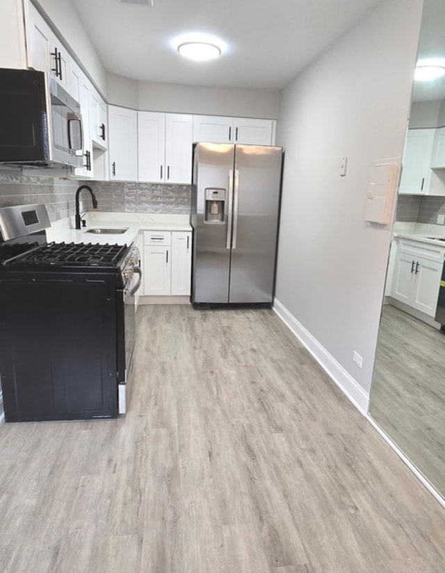 kitchen featuring appliances with stainless steel finishes, tasteful backsplash, sink, light hardwood / wood-style flooring, and white cabinets