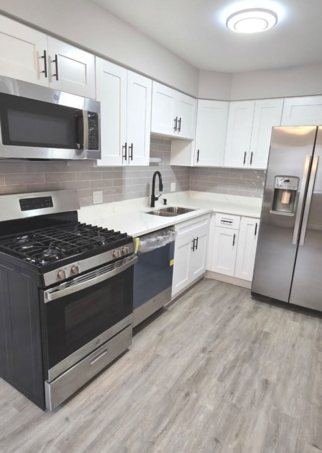 kitchen with white cabinets, sink, light hardwood / wood-style flooring, decorative backsplash, and stainless steel appliances