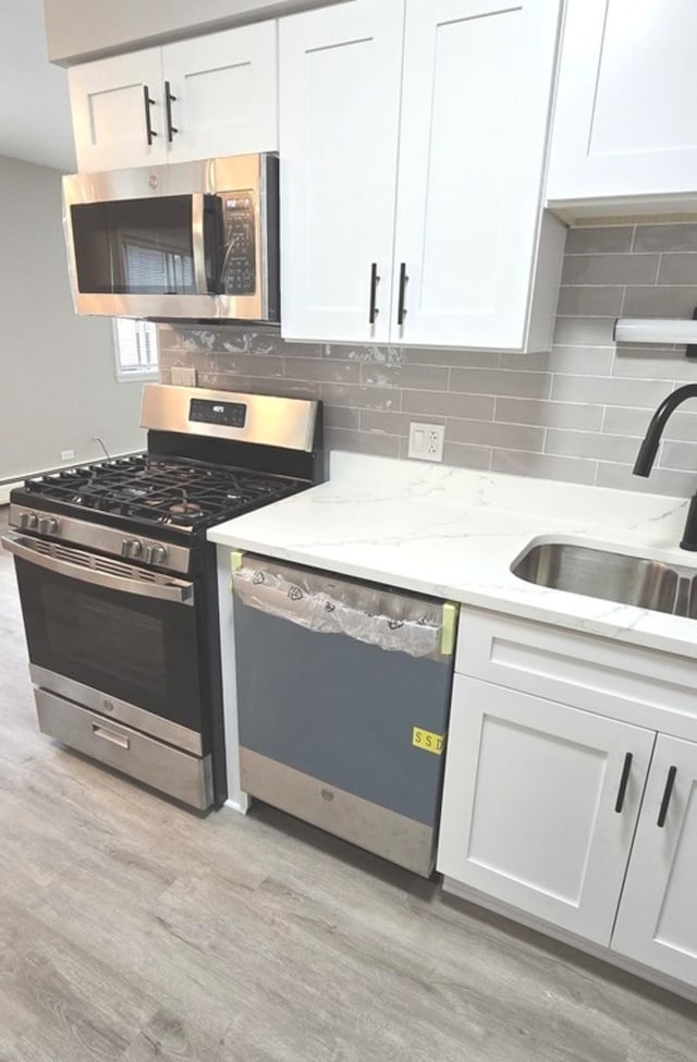 kitchen with white cabinets, light stone counters, appliances with stainless steel finishes, and light hardwood / wood-style flooring