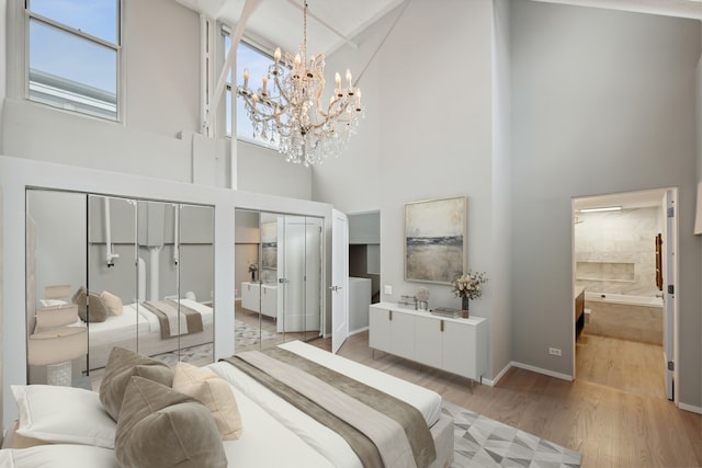 bedroom with a high ceiling, an inviting chandelier, two closets, ensuite bathroom, and wood-type flooring