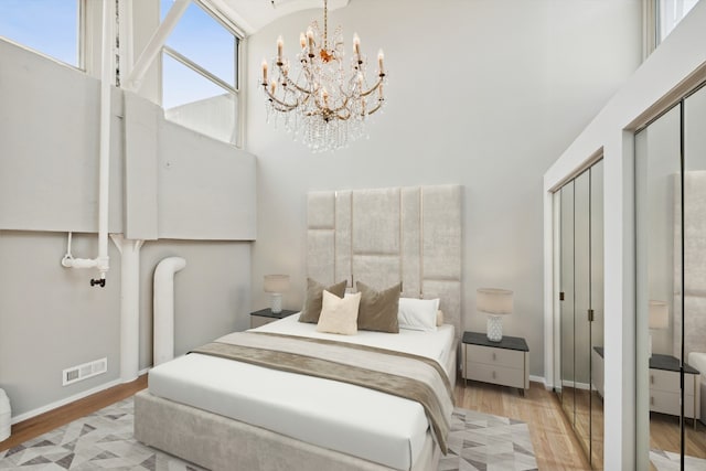 bedroom with a high ceiling, light wood-type flooring, two closets, and a notable chandelier